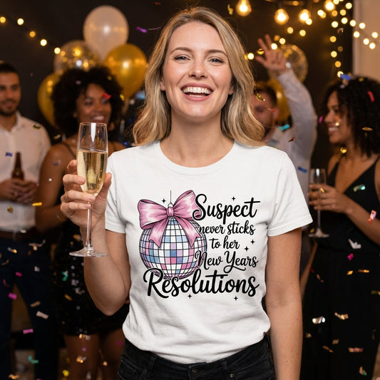Suspect Never Sticks to Her New Year's Resolutions DTF transfer design mockup on a white t-shirt featuring a pastel disco ball with pink bow and black script typography