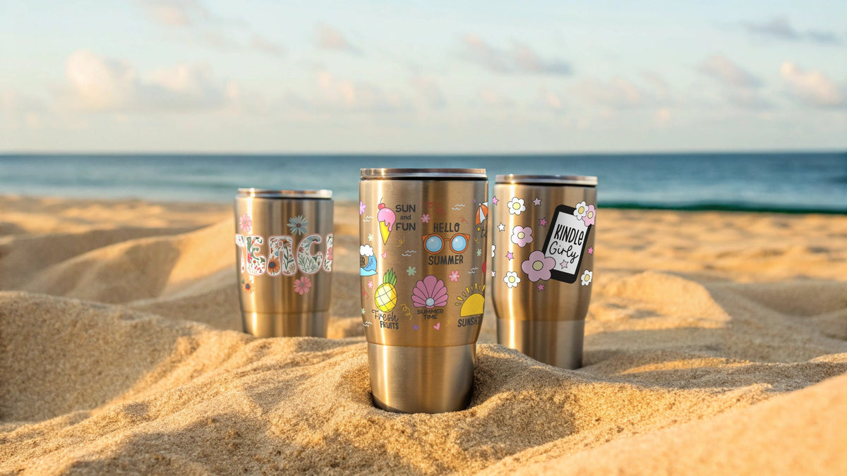 What Are UV DTF Stickers article header featuring three stainless steel tumbler cups decorated with colorful floral UV DTF transfer stickers set in beach sand at sunset