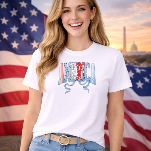 Coquette America DTF transfer design mockup on a t-shirt featuring AMERICA in patriotic patterned letters with a blue coquette ribbon bow