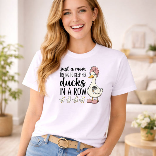 Just A Mom Trying To Keep Her Ducks In A Row DTF transfer design mockup on a t-shirt featuring a tired mama duck in a robe with hair towel and four ducklings in a line