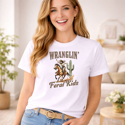 Wranglin' Feral Kids DTF transfer design mockup on a t-shirt featuring a cowgirl on horseback with cactus and rustic WRANGLIN Feral Kids lettering